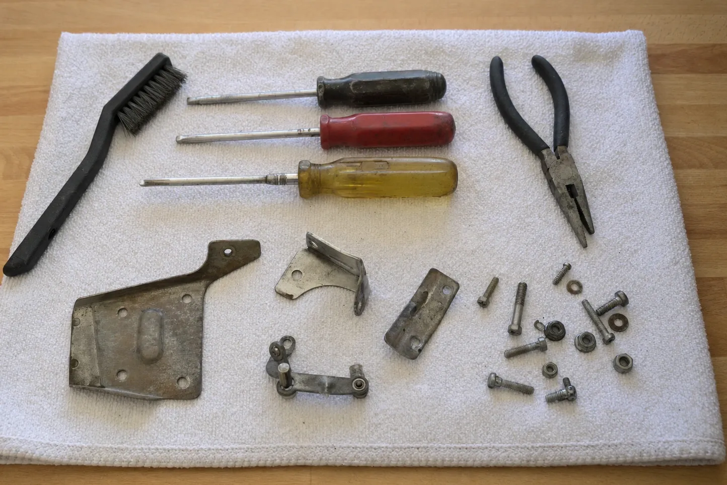 Appliance door hinge plate, brackets and a linkage laid out with a wire brush, pliers, drivers and fixings